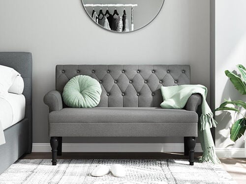 Sof&aacute; gris tapizado de 2 plazas en un dormitorio decorado. Haz clic para ver los productos.