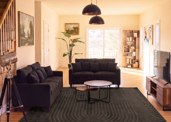 Sal&oacute;n moderno con dos sof&aacute;s oscuros, mesas de centro nido, mueble de TV y una alfombra grande en un espacio luminoso.
