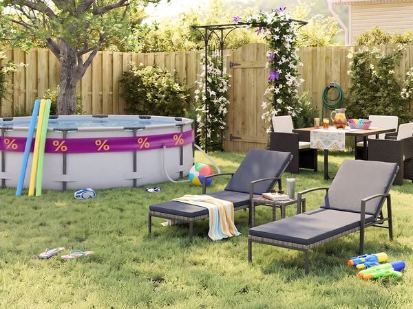 Jard&iacute;n trasero soleado con piscina elevada, churros de piscina, gafas de nataci&oacute;n, pelota de playa y chanclas sobre el c&eacute;sped. Dos tumbonas negras de metal con cojines grises se sit&uacute;an junto a una peque&ntilde;a mesa auxiliar, mientras un comedor de exterior con sillas oscuras de rat&aacute;n queda junto a una p&eacute;rgola con flores, una valla de madera y plantas de jard&iacute;n.