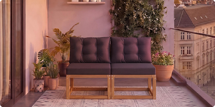 Sofá modular de madera de dos plazas con cojines gris oscuro en un balcón rodeado de plantas en maceta y vistas a la ciudad al fondo