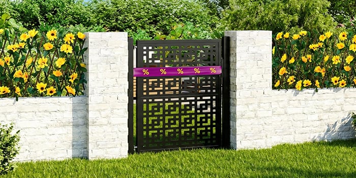 Puerta de jardín de metal negro envuelta en una cinta de descuento morada y amarilla, enmarcada por una valla de hormigón blanco con flores y vegetación al fondo. Haz clic para ver los productos de la oferta.