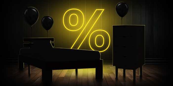 Cama negra y cómoda con globos negros frente a un letrero de porcentaje amarillo brillante sobre un suelo de madera oscura.