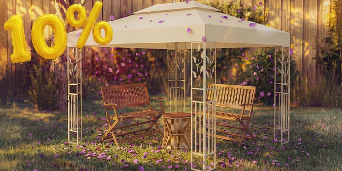 Cenador de jardín con dos bancos de madera y una pequeña mesa debajo, rodeado de confeti rosa y globos dorados con «10 % de descuento», que destaca una oferta de temporada en cenadores y toldos de jardín.