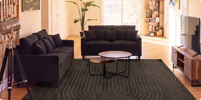 Salón moderno con dos sofás oscuros, mesas de centro nido, mueble de TV y una alfombra grande en un espacio luminoso.