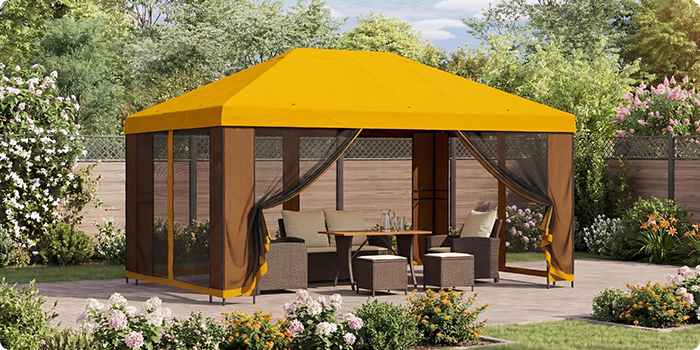 Cenador de jardín amarillo con cortinas de malla que cubre un conjunto de asientos con mesa en un patio, rodeado de plantas en flor en un entorno soleado.